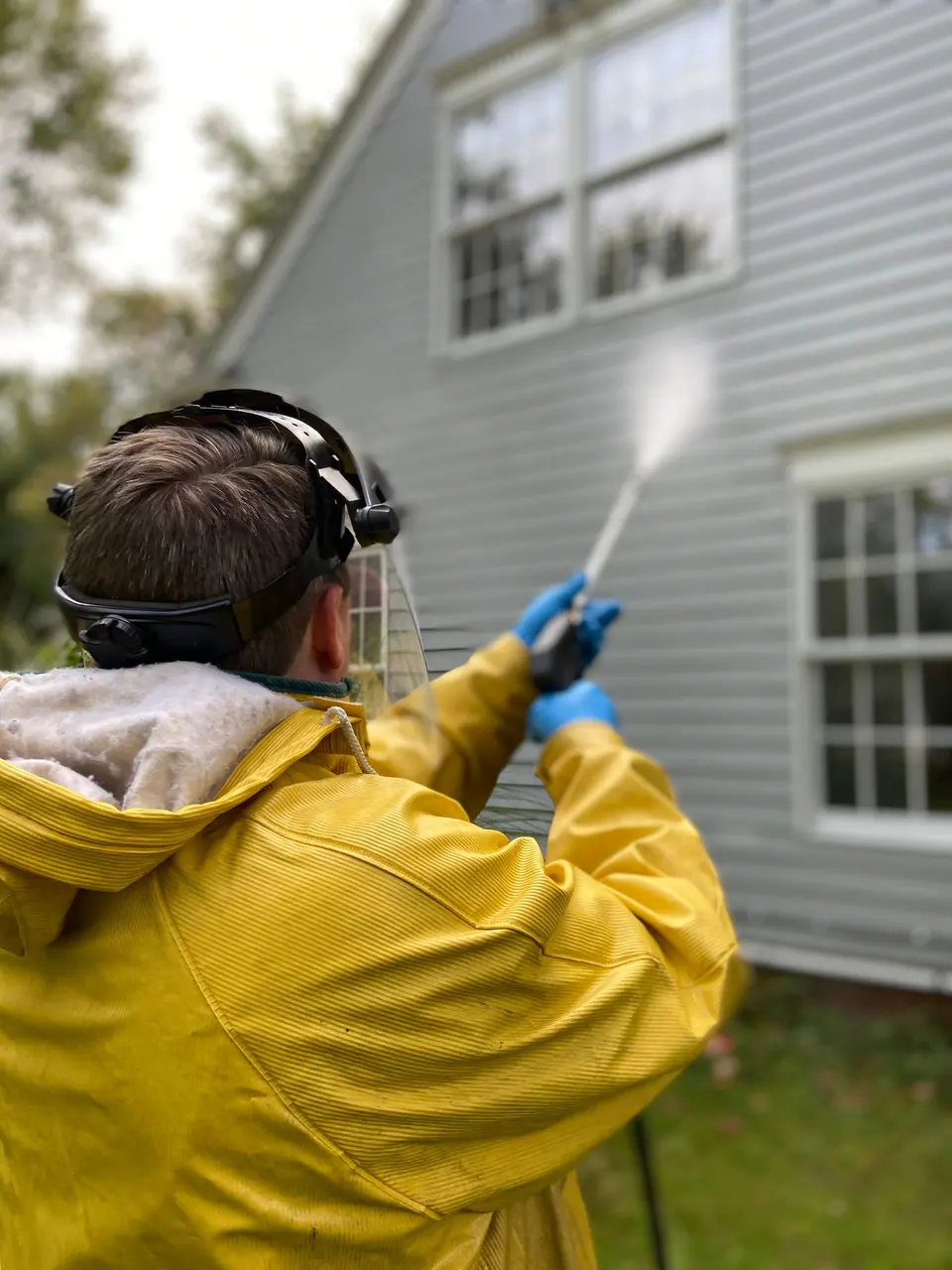 Power washing white clapboard siding on a house exterior